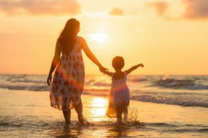 夕焼けの海で子供の手を引くお母さん、神仏の見守りをイメージ