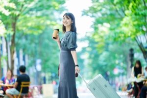 笑顔でスーツケースを引く女性。推し活で遠征を楽しむ女性のイメージ